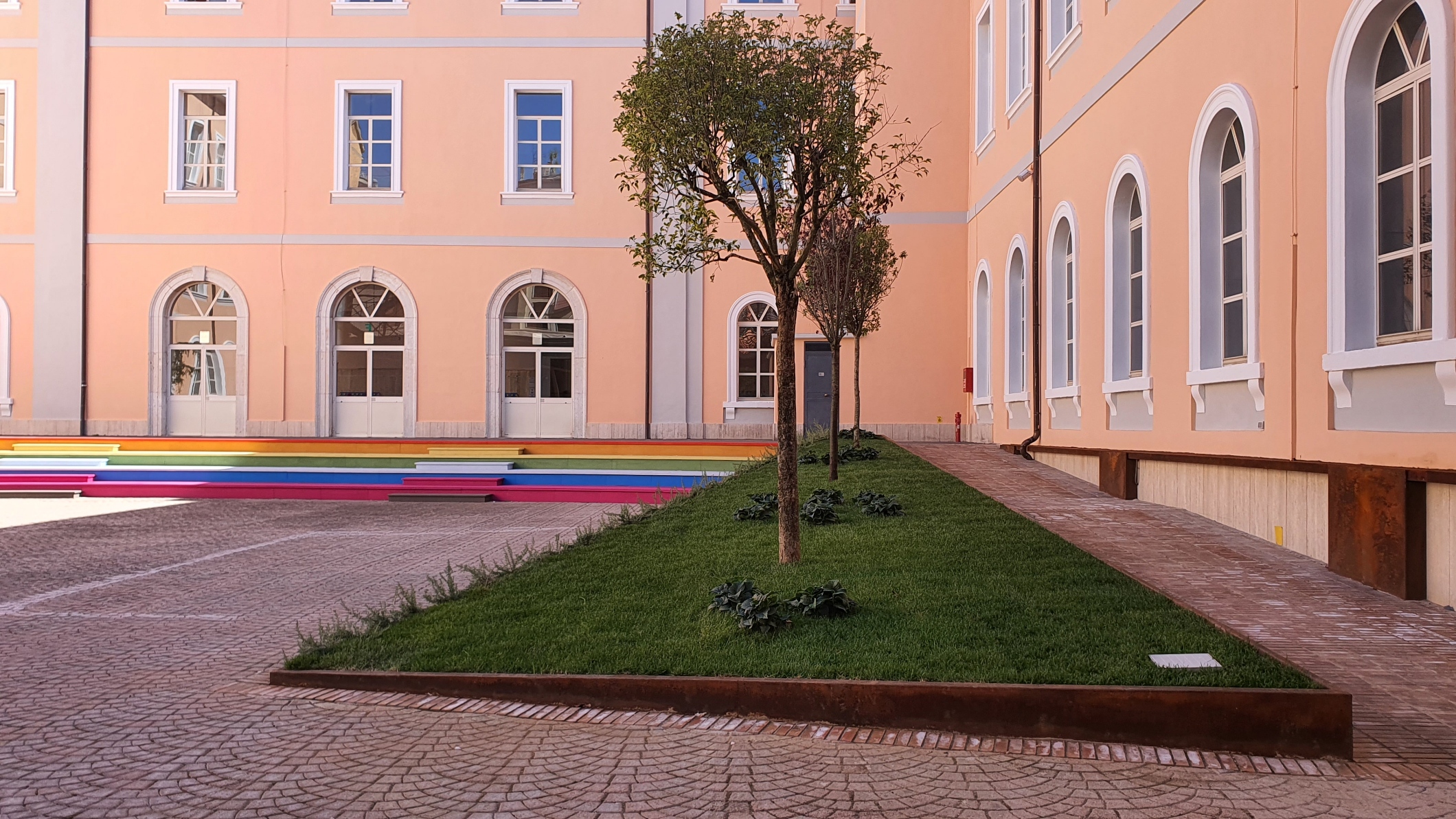 Fioriera inclinata con alberi e verde che accompagna la rampa accessibile nella corte del Palazzotto
